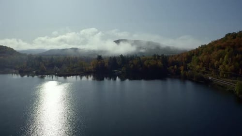 An idyllic autumn scene featuring a still lake reflecting sunlight and surrounding vibrant fall foli