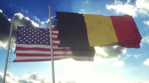 USA and Belgium Flags Waving Against Sunny Blue Sky