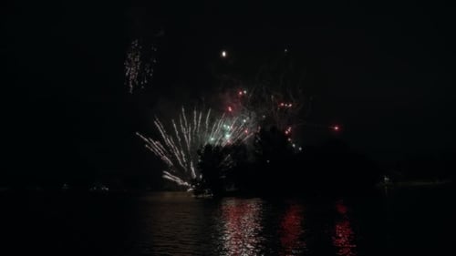 Colorful fireworks behind the trees reflecting n the lake water
