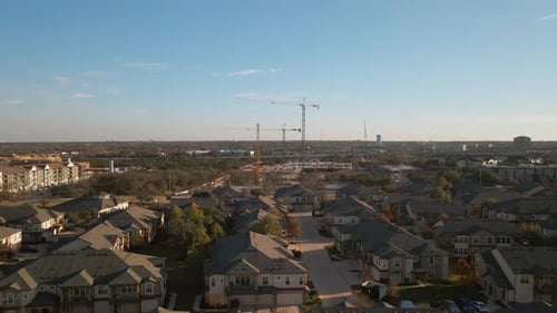 Aerial view of multiple construction cranes at construction site fill the blue sky near a neighborho