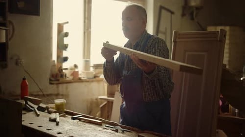 Senior Man Blowing Out Sawdust in Carpentry Workshop. Closeup Focused Carpenter Cleaning