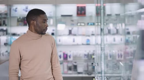 An African Man Walks Along the Glowing Windows in an Electronics Store