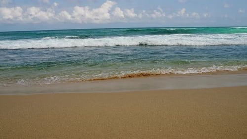 Les vagues s'écrasent sur une plage de sable par temps clair : le sable chaud rencontre la mer turquoise et ses calottes blanches