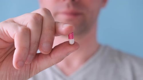 Adult Holding and Taking a Pink and White Capsule