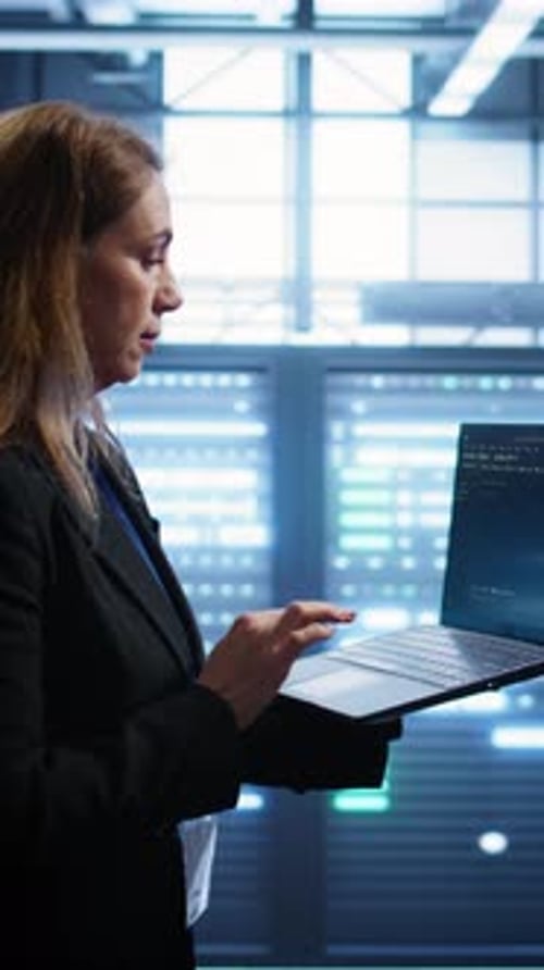 Vertical Video Woman Walking in High Tech Facility Using Laptop to Patch Network Issues