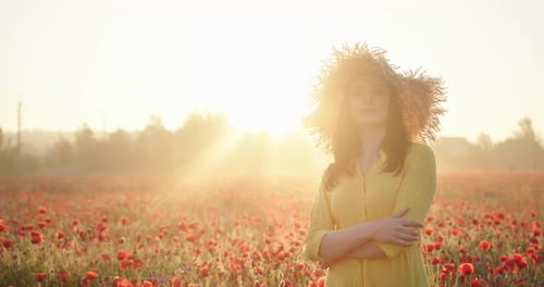 Brunette Woman in a Yellow Dress and Straw Hat in Poppy Field at Sunrise