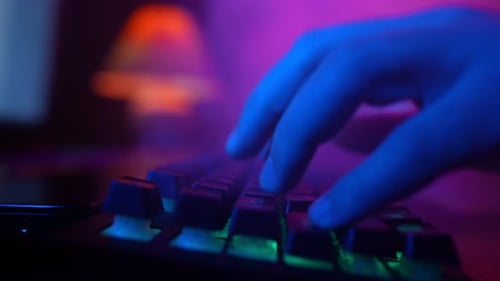 Male Hands Typing on Computer Keyboard in Neon Lighting