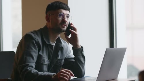 Freelancer in Glasses Working with Laptop and Talking on the Phone in Cafe Indoor Footage of Stylish