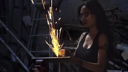 A young Asian female mechanic welding auto parts in a repair garage.