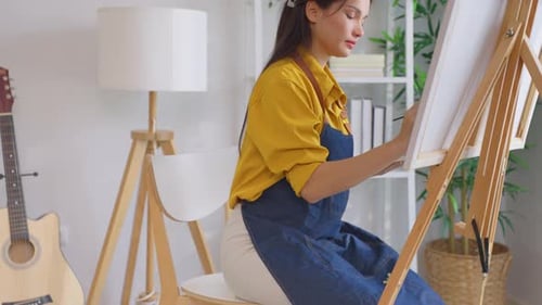 Asian young talented woman artist coloring on painting board in house.