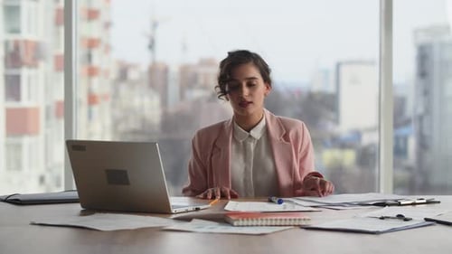 A Businessman Sits in His Office in Front of a Large Window and Sorts Through the Company's
