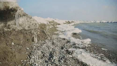 Costa helada con carámbanos en las rocas en medio de las olas del mar en un soleado día de invierno. - Toma estática