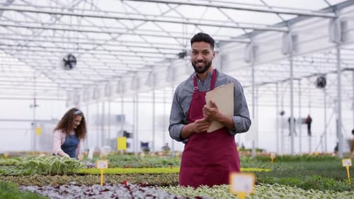 Colleagues Working in Garden Centre, Man with Board Looking at Camera