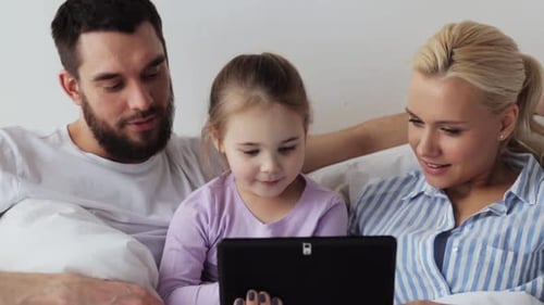 Family using tablet in bed, smiling, enjoying technology