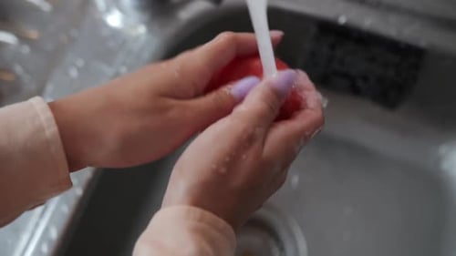Washing Fresh Tomato Under Running Water in Kitchen Sink