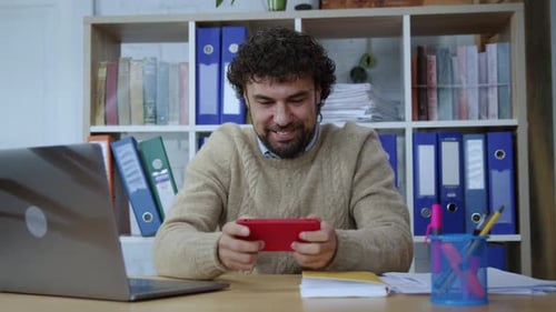 Empleado de oficina que juega un juego de aplicaciones móviles en un teléfono inteligente, gana y se anima durante las vacaciones