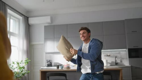 Young Couple Enjoying Playful Pillow Fight at Home
