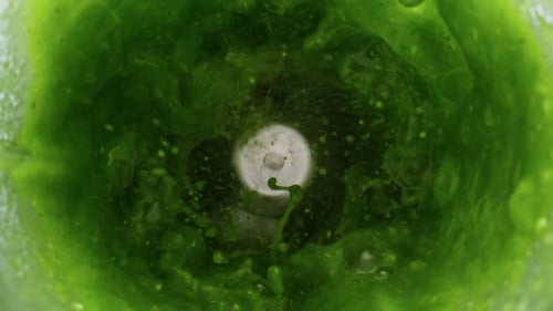 Glass blender mixing green vegetable smoothie blend in super slow motion close up view