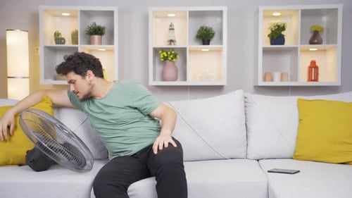 Man overwhelmed by hot air cools down with fan.