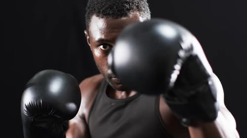 Focused African American boxer training in a dark gym on a black background