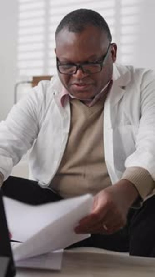 Vertical Portrait of Professional Doctor in White Gown Viewing Papers with Blood Test Results
