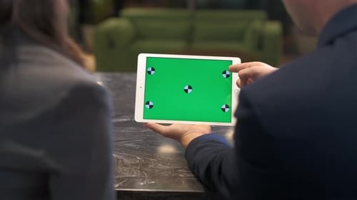 A man and a woman sit at an office desk and discuss information on the tablet.