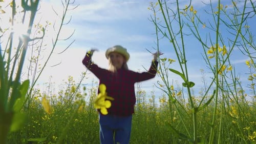 Girl Jumps Up During the Day in the Sun in the Field of Yellow Rapeseed
