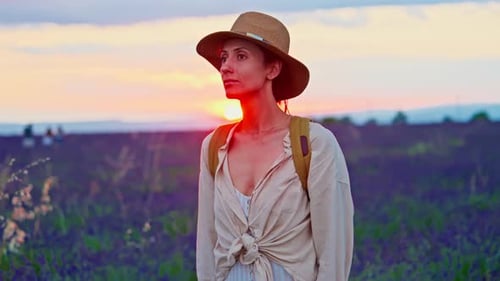 Une touriste avec un chapeau et un sac à dos se promène dans un champ de lavande pendant un magnifique coucher de soleil à
