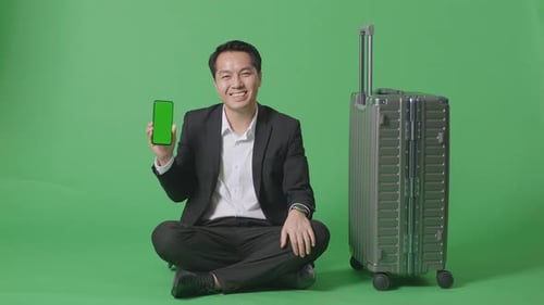 Businessman With Luggage Smiling And Showing Green Screen Smartphone In The Green Screen