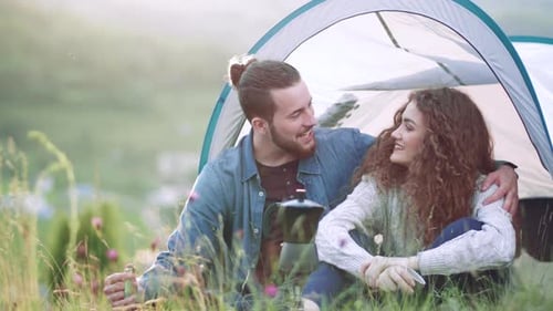 Young couple resting in nature near tent shelter on summer holiday