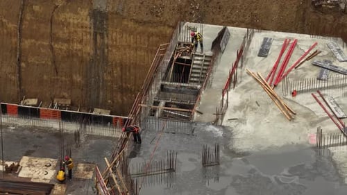 Aerial close up of construction workers reinforcing concrete foundation walls with rebar and formwor