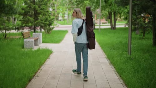 Busker in Urban Park Heading Forward Indie Artist Walking Through City Green Spaces Guitar Player