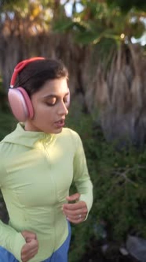 Woman Jogging in Tropical Park Wearing Headphones
