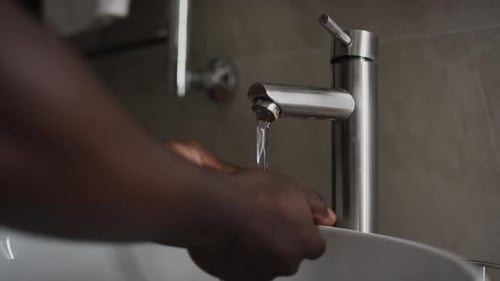 Joven negro anónimo lavándose las manos en el lavabo del baño