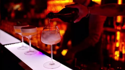 Barman making a cocktail with white sparkling wine at the bar at night with red neon lights, slow mo