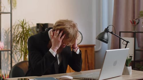 Worried Man at Desk with Laptop Expressing Disappointment