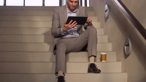 Businessman with tablet drinking coffee on office stairs technology concept