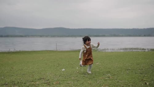 slow motion of toddler girl running on a grass field near the river
