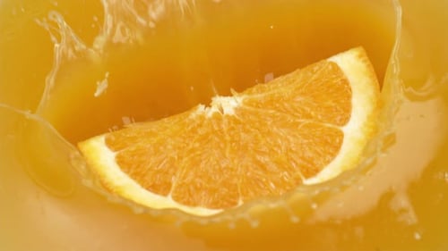 Orange slice plunges into refreshing orange juice creating a vibrant splash in slow motion