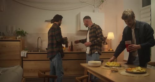 Trio de amigos felizes em camisetas colocando bebidas e lanches na mesa antes da despedida de solteiro