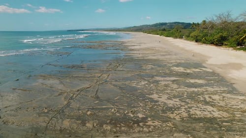 Aerial view of wide sandy beach with tidal rock patterns and distant hills