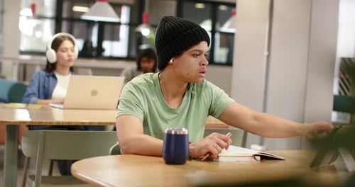 Adult African American man glancing at tablet, tapping stand, writing notes while studying at desk
