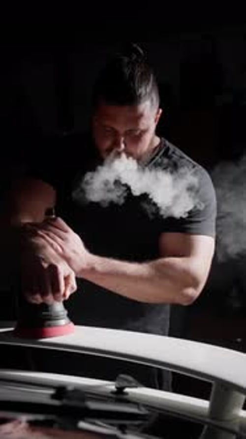 A Man Polishes a Car and Smokes an Electronic Cigarette