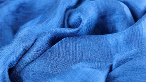 Close-up view of soft folds of dark blue silk muslin rotated on the display case. Textile background