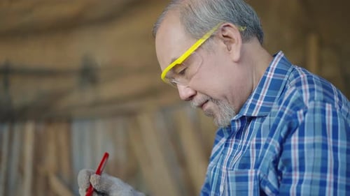Asian senior carpenter using ruler to measuring wood board at the carpentry workshop.