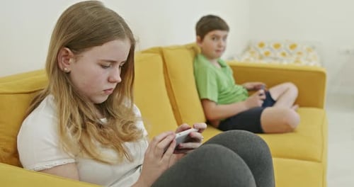 Teen Girl and Boy Using Devices on Couch