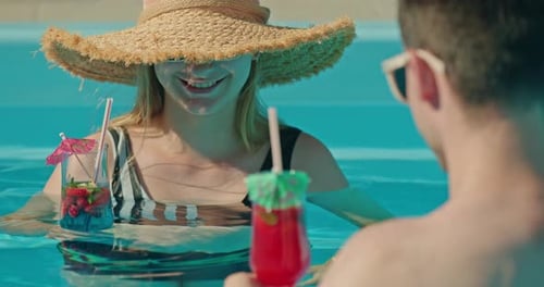 Young Couple Enjoying Tropical Cocktails While Relaxing in a Swimming Pool on a Sunny Vacation Day