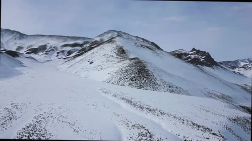 Aerial view drone flying over beautiful white snowy mountains landscape and a cloudy sky.