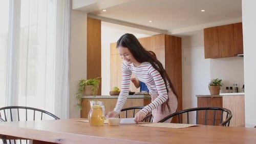 Woman Setting Table While Another Prepares Food