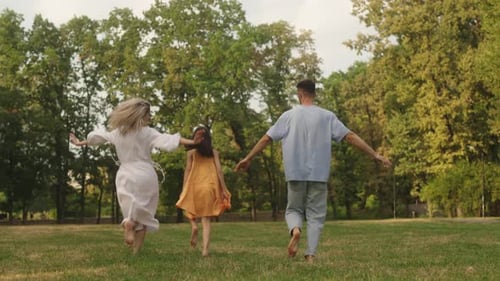 Happy Family Running Through Park Holding Hands Barefoot on Grass Summer Fun